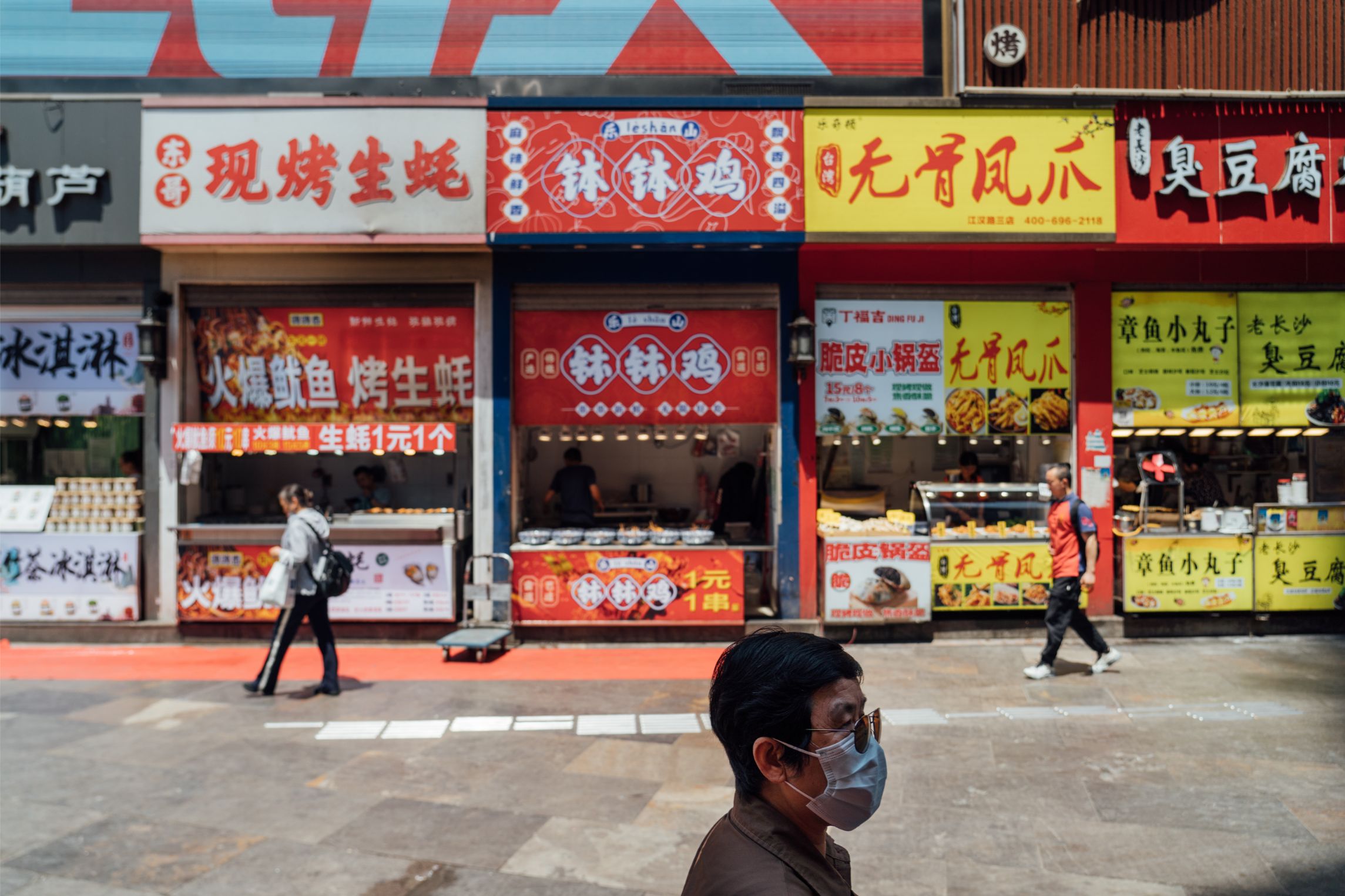Photo of a pedestrian walking in front of local food stalls in Wuhan.